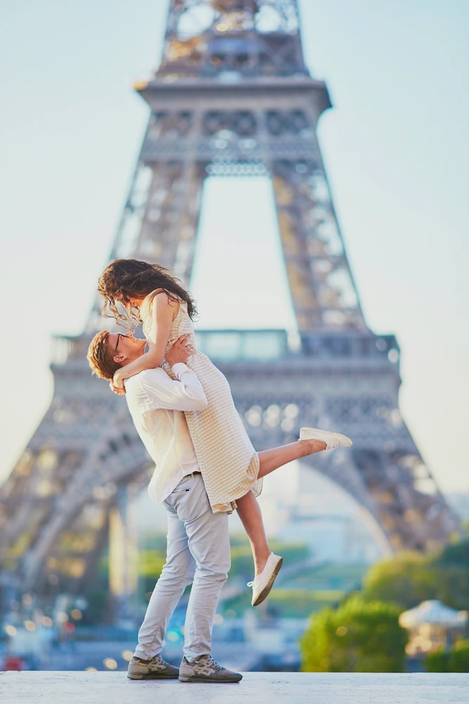 Couple d’amoureux heureux près de la tour Eiffel à Paris, symbole du romantisme et parfait décor pour un week-end en amoureux dans la capitale. Photo publiée sur monsieurdefrance.com.
