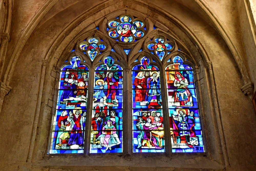Colorful stained glass windows in the church of Gournay-en-Bray, filtered light and religious motifs