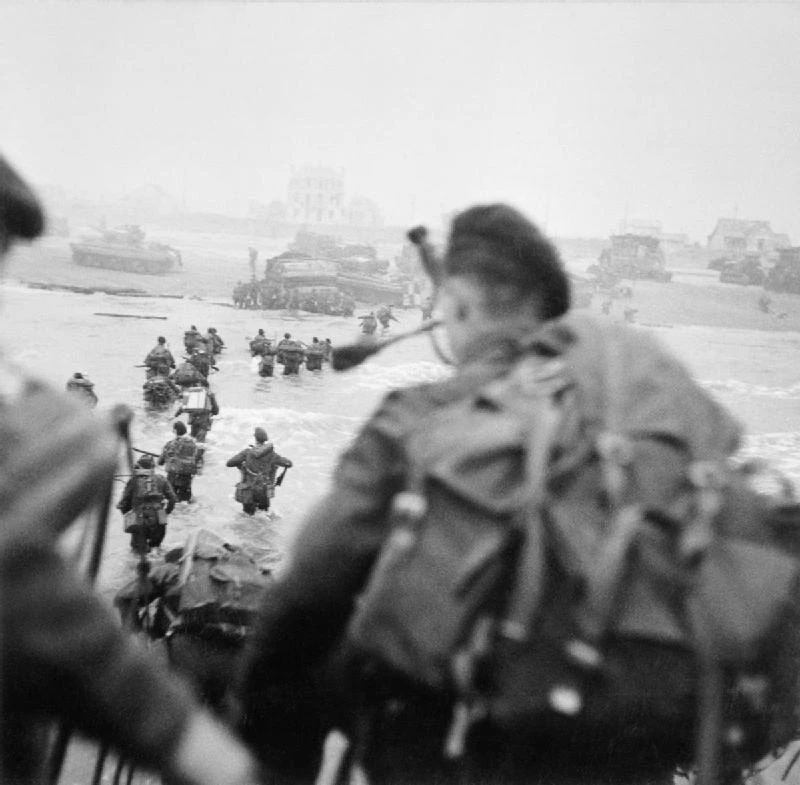 Les soldats britanniques et français débarquent sur Sword beach au son de la cornemuse du piper Bill Milin (sur la droite). Source de Monsieurdefrance.com : Domaine public américain via Wikipedia.
